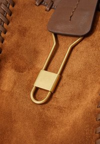 Bruin suede materiaal met een gladde textuur, voorzien van een gouden metalen sluiting en leren details, met ingewikkelde stiksels.