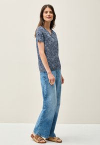 Maglietta blu navy a maniche corte con un motivo ondulato bianco, abbinata a jeans a gamba larga azzurri e sandali intrecciati beige.
