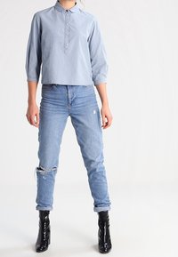 Ljusblå, kragig, knapplång blus med prickigt mönster. Bärs med slitna, ljusblå jeans och glänsande svarta ankelskor.