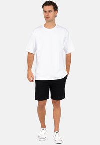 Witte katoenen T-shirt met een ronde hals, gecombineerd met zwarte shorts. Witte sneakers maken de outfit compleet, met een eenvoudig ontwerp en een casual pasvorm.