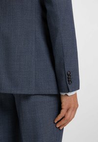Marine pakkenjasje met een gestructureerde stof, slim fit, vier zwarte knopen op de manchetten en een zichtbaar lichtblauw shirt onder de mouw.