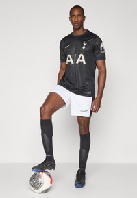 Melnā Nike futbolista krekls ar "AIA" logotipu, apvienots ar baltām biksēm. Melni zābaki ar pelēkiem akcentiem un melnām botām. Futbola bumba pie kājām.