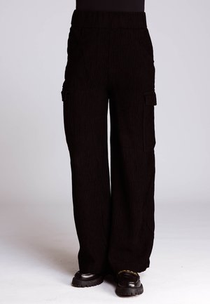 Schwarze Cordhose mit weitem Bein und hohem Bund, mit einer seitlichen Cargo-Tasche und vertikaler Rippstruktur. Schuhe sind nicht enthalten.