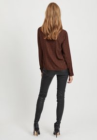 Brun mönstrad långärmad blus i kombination med åtsittande svarta byxor och svarta ankelboots med klack. Slät tygkvalitet med en avslappnad passform.