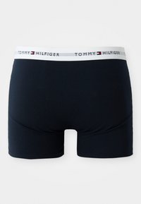 Boxeri bărbătești bleu marin dintr-un material neted, cu un elastic alb pe care este inscripționat logo-ul "Tommy Hilfiger" în culorile negru și roșu.