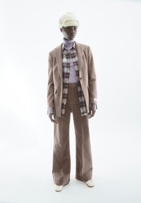 Bruine getextureerde blazer over een geruit overhemd, gelaagd met een paarse coltrui. Wijdbeige broek en roomkleurige laarzen maken de outfit compleet.