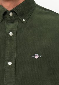Groene corduroy blouse met een button-down kraag, voorzien van witte knopen en een klein geborduurd logo op de borst. Gestructureerde stof.