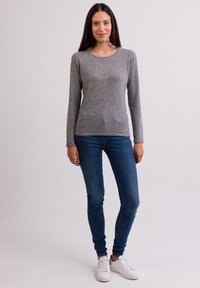 Graues Langarmoberteil aus weichem Material, kombiniert mit blauen Skinny-Jeans und weißen Sneakers. Einfacher runder Halsausschnitt und figurbetonter Schnitt.