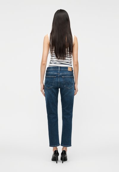 Traperice tamnoplave boje s visokim strukom i ravnim krojem nogavica. Imaju stražnje džepove i smeđu kožnu oznaku iznad desnog džepa.