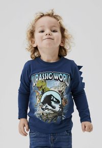 Hosszú ujjú tengerészkék ing, élénk Jurassic World grafikával, amely dinoszauruszokat és egy kerek logót ábrázol; tüskés részletek a vállaknál.