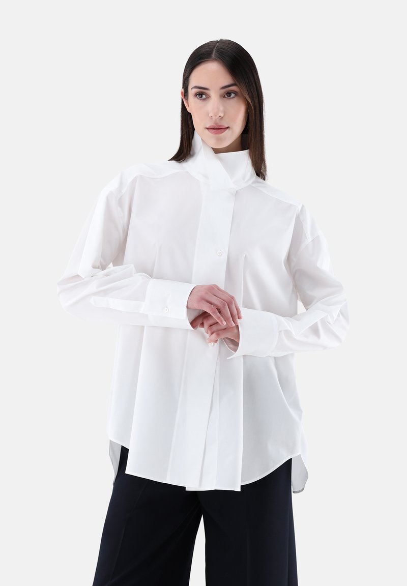 Camicia bianca a maniche lunghe con colletto alto, realizzata in un tessuto liscio, con chiusura frontale con bottoni e dettagli sul patta, vestibilità ampia e spacchi laterali.