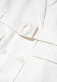 Biały żakiet z tkaniny z paskiem z kwadratową klamrą. Teksturowany materiał, widoczne guziki i podwójne przednie kieszenie. Miękkie wykończenie.