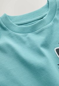 Jasnoniebieski sweter z okrągłym dekoltem, z prążkowanym kołnierzem i częściowo haftowanym wzorem w czerni i bieli po boku.