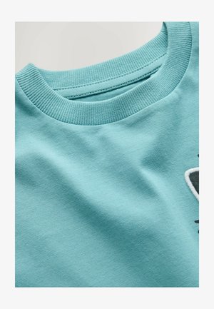 Sweat-shirt bleu clair à col ras du cou avec col en côte et design brodé partiel en noir et blanc sur le côté.