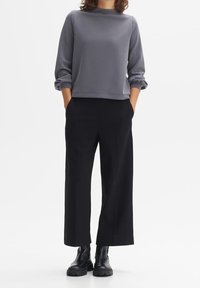 Sudadera gris con un escote redondo y mangas enrolladas, combinada con pantalones de pierna ancha negros y botas gruesas negras.