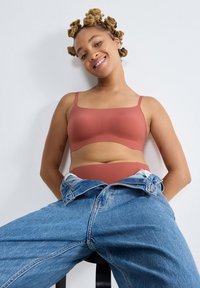 Roze naadloze beha en bijpassende slip, gemaakt van glad materiaal, gecombineerd met ongeknopte lichtblauwe denim jeans.