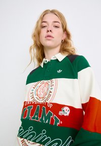 Zaļš, sarkans un balts svītrots kokvilnas polo krekls ar apkaklīti, ar "Miami universitātes" grafiku un Adidas logotipu.