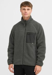 Graue Fleecejacke mit hohem Kragen, Reißverschluss-Brusttasche und schwarzen Akzenten. Verfügt über einen strukturierten Stoff und eine lockere Passform.