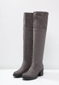 Graue Overknee-Stiefel aus weichem Wildleder, mit Blockabsatz und Gummisohle, sowie gesteppten Akzenten an den Seiten.