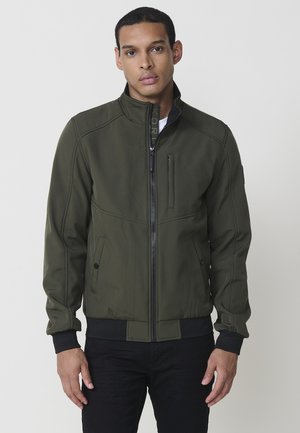 Chaqueta bomber verde oliva con cuello alto, cierre frontal con cremallera, bolsillos laterales y puños y dobladillo acanalados negros en contraste. Presenta detalles de costura sutiles.