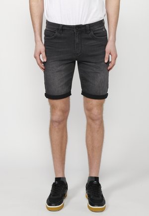 Shorts di jeans neri con orli risvoltati, cinque tasche e una leggera texture sbiadita. Abbinati a sneaker nere e una maglietta bianca.