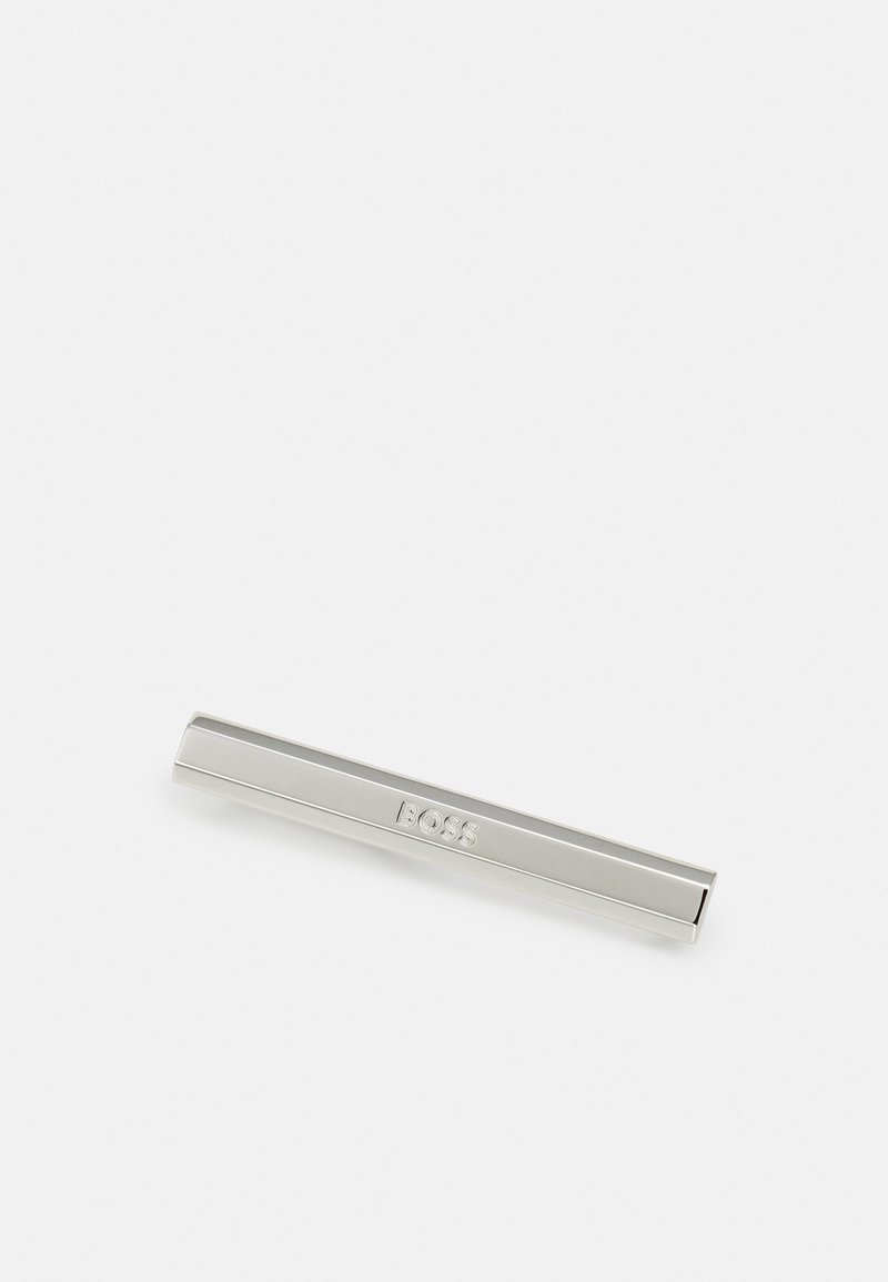 Pince à cravate en métal argenté, forme rectangulaire avec finition lisse. Logo "BOSS" gravé dans une police simple. Design minimaliste.