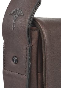 Angolo di una borsa in pelle marrone con design impresso e cucitura a contrasto. Include un dettaglio con bottone metallico e una morbida fodera interna.