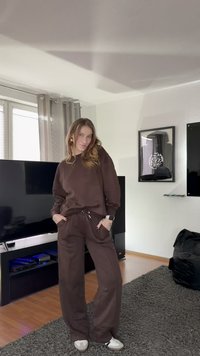 Hnědá mikina a odpovídající volné kalhoty, obojí z měkké látky. Pár bílých tenisek, volný střih, v pohodovém vnitřním prostředí.