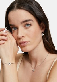 Silberne Schmuckstücke mit einem Cluster-Design, das drei kugelförmige Perlen umfasst; beinhaltet passende Ohrringe, ein Armband und eine Halskette auf heller Hintergrund.