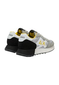 Zapatillas grises y blancas con acentos en negro y amarillo, materiales de ante y malla, forma redondeada y suelas estratificadas para mayor amortiguación.