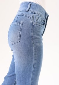 Pantalones vaqueros de denim azul con un ajuste slim, cintura de altura media y dos bolsillos traseros con detalles de costura minimalistas. Textura suave y acabado liso.