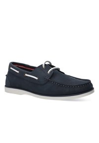 Marineblaue Wildleder-Bootsschuhe mit weißen Schnürsenkeln und Metallösen. Kontrastnähte und eine weiße Gummisohle. Das Innere hat ein rot gemustertes Futter.