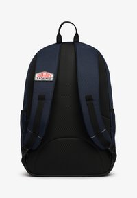 Mochila azul marino con un respaldo de malla negra texturizada, correas ajustables y un prominente parche con el logotipo "Superdry Machined" en la parte frontal.