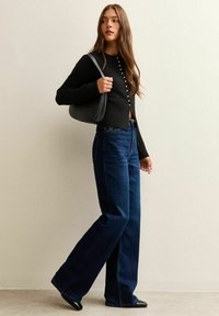Svart långärmad cardigan med knapppaket, parat med högmidjade, vida mörkblå denimjeans och en svart axelväska.