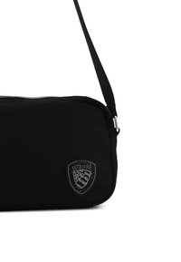 Borsa a tracolla nera con una texture liscia, dotata di chiusura a zip e una patch a forma di scudo con dettagli scintillanti. Inclusa una tracolla regolabile.