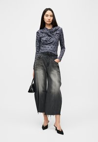 Γκρι μπλούζα με πουά και μακριά μανίκια, με σχέδιο μπροστινού κόμπου, συνδυασμένη με φαρδιά ξεβαμμένα μαύρα τζιν και μαύρες μυτερές γόβες.