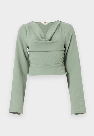 Przycięta bluzka z długim rękawem w miękkim, teksturowanym miętowym materiale. Posiada lejący dekolt typu cowl oraz dopasowany krój, z poziomą detalem szwu.