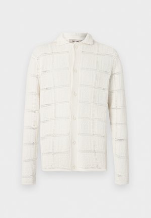 Cardigan blanc à manches longues avec boutons, motif carré texturé et col, présenté sur un fond uni.