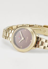 Gold-tone wristwatch with a round case, brown glitter dial, gold hands, and a polished bracelet strap. Features logo detail on the dial.