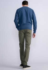 Conjunto casual para hombre que incluye un sudadera azul, pantalones verde oliva y zapatillas negras con suelas blancas. Tejido suave y diseño sencillo.