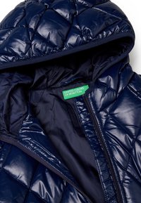 Náměstí modrá prošívaná péřová bunda s kapucí, se lesklým povrchem a zeleným štítkem uvnitř, na kterém je uvedeno "United Colors of Benetton."