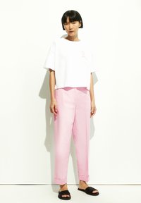 Witte cropped t-shirt met een roze lintontwerp, gecombineerd met lichtroze wijde broek met opgerolde mouwen en zwarte instapsandalen.