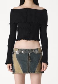 Haut noir côtelé à épaules dénudées avec bords à volants, associé à une mini-jupe en jean patchwork avec une fermeture éclair et une ceinture à accent métallique.