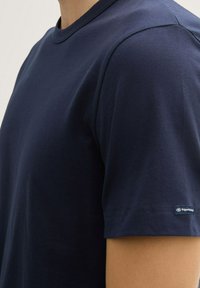 T-shirt in cotone blu navy con collo rotondo, maniche corte e un piccolo etichetta di marca sulla manica sinistra. Tessuto morbido e vestibilità casual.