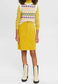 Jupe en velours côtelé jaune associée à un gilet en tricot crème et à motifs. Des bottines noires et crème complètent la tenue.