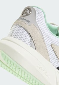 Białe sneakersy z siateczki z szarymi zamszowymi akcentami, miętowymi detalami i fakturowaną miętową gumową podeszwą. Posiadają srebrne logo AMG na pięcie.