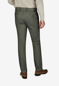Graue Hose aus einem strukturierten Stoff, mit geradem Bein design, Gesäßtaschen mit Knöpfen und einem dezenten Muster. Braune Schuhe getragen.