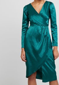 Teal Satin-Wickelkleid mit langen Ärmeln, das mit einem dezenten Tierdruck, V-Ausschnitt und einem seitlichen Schlitz für zusätzlichen Detailreichtum und Bewegung versehen ist.