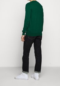 Grön stickad tröja med långa ärmar, rundad halsringning, parat med mörk denimjeans och vita högskurna sneakers. Enkel, avslappnad design.