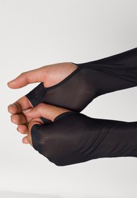 Mănuși negre, ajustate, fără degete, realizate dintr-un material neted și elastic, cu cusături evidente și deschideri pentru degetul mare și încheietură, care îmbunătățesc dexteritatea.